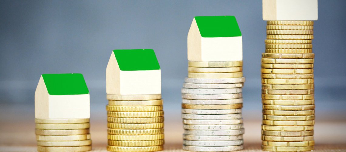 Rising cost of houses, real estate concept, with stack of coins and small wooden houses